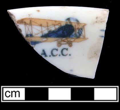 Hollow vessel of indeterminate form with rolled rim and decal motif of airplane and letters “A.C.C.” Rim diameter: 5.00”; 5.0 mm thick. Possibly Alaska Commercial Company (1890-1923).  (Hunter Research Poster)